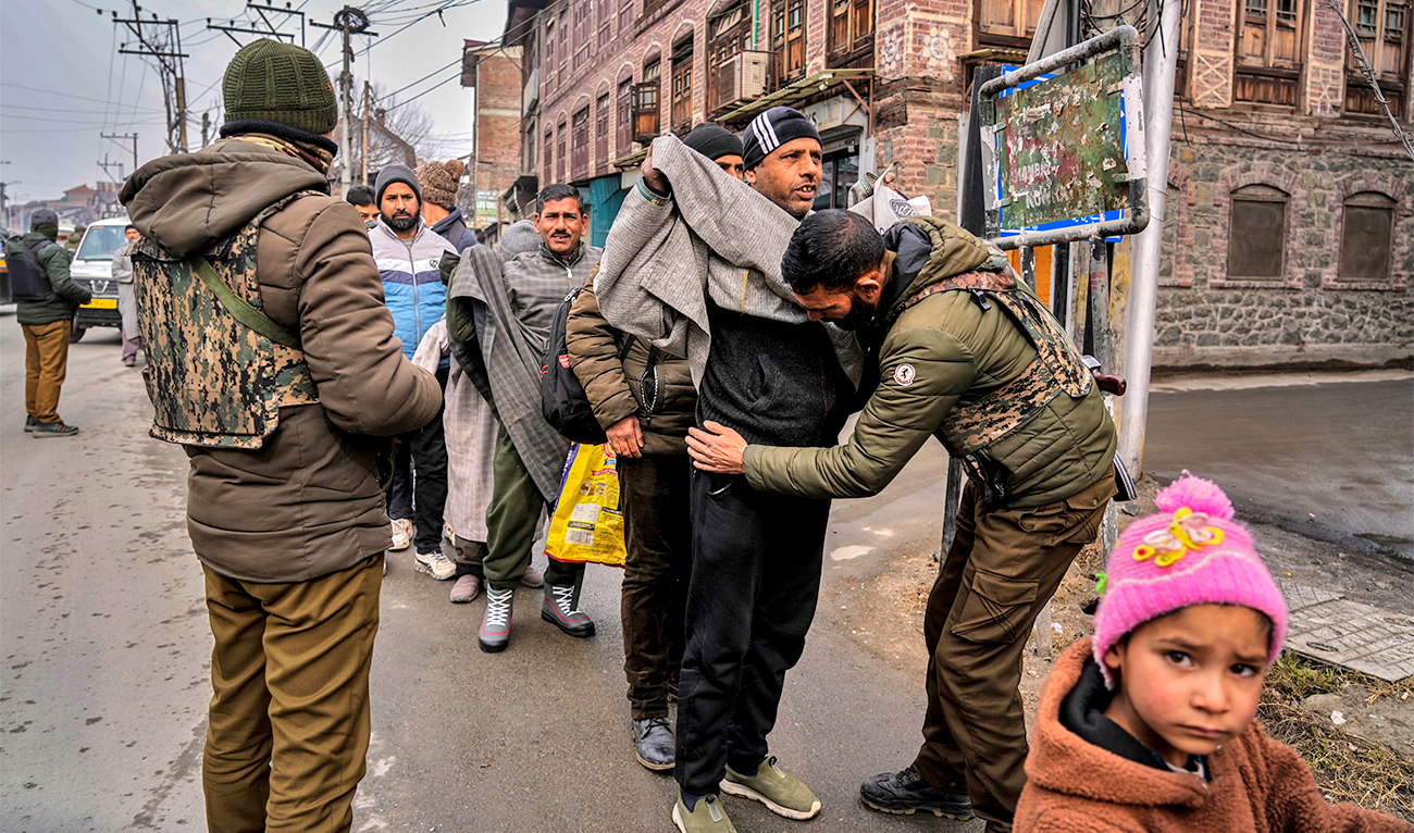 A child looks on as Indian policemen frisk Kashmiri pedestrians during a surprise security check in Srinagar, Indian controlled Kashmir, on January 9, 2023. (AP)