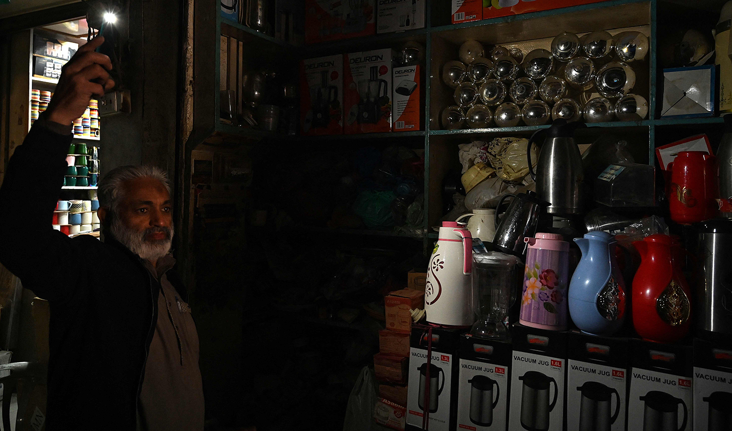 A shopkeeper uses his mobile phone's torch light at a market during a nationwide power outage in Rawalpindi, Pakistan, on January 23, 2023. (AFP)