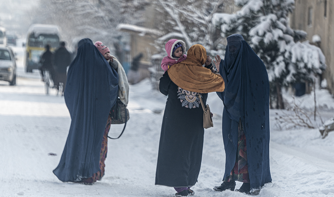 In this file photo taken on January 23, 2023, Afghan burqa-clad women carry children as they walk along a snow laden street in Kabul. (Photo courtesy: AFP/File)