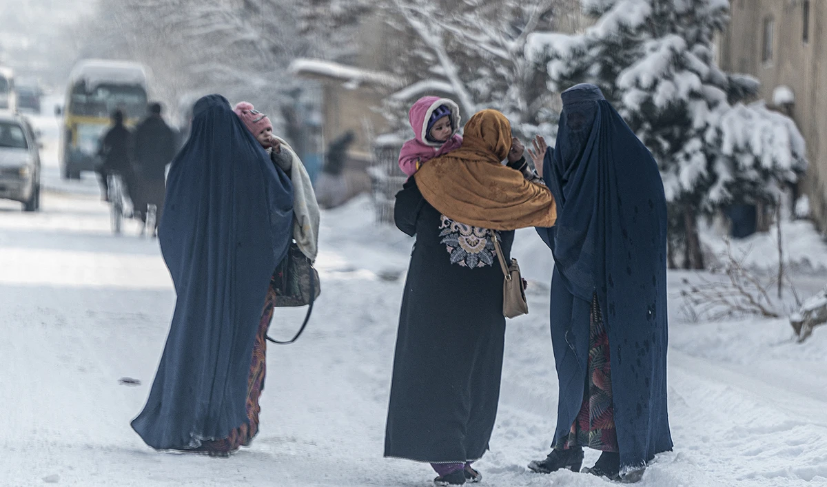 In this file photo taken on January 23, 2023, Afghan burqa-clad women carry children as they walk along a snow laden street in Kabul. (Photo courtesy: AFP/File)