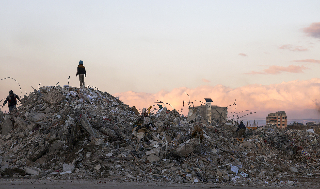 Syrians search building rubble for items to salvage in the regime-controlled town of Jableh in the province of Latakia, northwest of the capital, on February 10, 2023, in the aftermath of a deadly earthquake. (Photo courtesy: AFP)