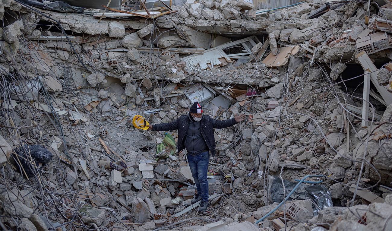 A man stands amid rubble of a collapsed buidling while Greek and Turkish rescuers try to exhume the bodies of six of his relatives, including four children in Antakya, south of Hatay, on February 15, 2023. (Photo courtesy: AFP)