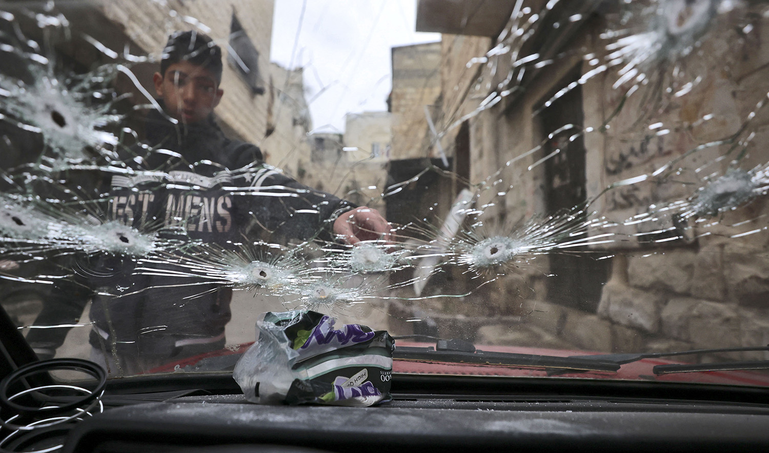 A Palestinian youth points at a bullet-riddled windshield outside a house that was targeted during an Israeli army raid in the Old City of Nablus the previous day, on February 23, 2023. (AFP)