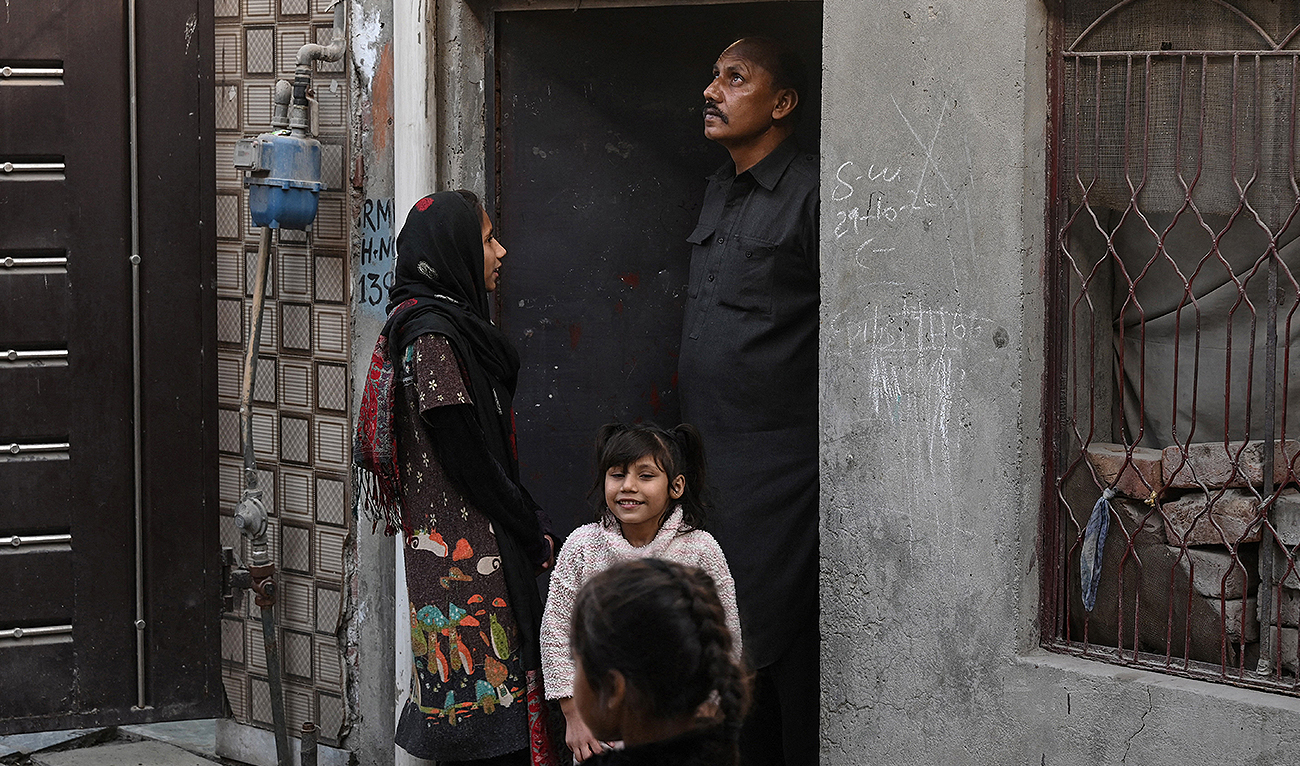 In this picture taken on February 12, 2023, Muhammad Amin, who works as a security guard, stands with his daughters outside their home in Lahore. (Photo courtesy: AFP)