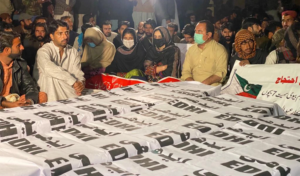 A group of protesters sit right next to the coffins of a woman and her two sons in Quetta, Pakistan, on February 22, 2023, accusing a provincial minister of triple murder and demanding his arrest. (@paank_bnm/Twitter)