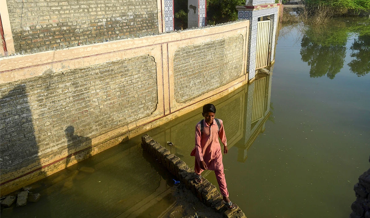 In this picture taken on October 28, 2022, a flood-affected student walks past a deluged government primary school in Chandan Mori, in Dadu district of Sindh province. (Photo courtesy: AFP)