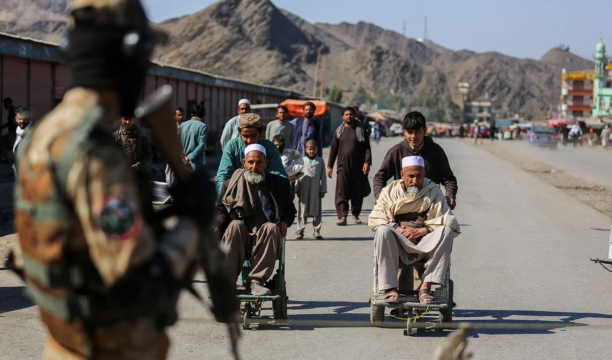 A Taliban security personnel stands guard as young Afghan boys help elderly men in wheelchairs after an incident of gunfire between Afghanistan and Pakistan border forces near the Torkham border crossing between Afghanistan and Pakistan, in Nangarhar province on February 20, 2023. (AFP/FILE)