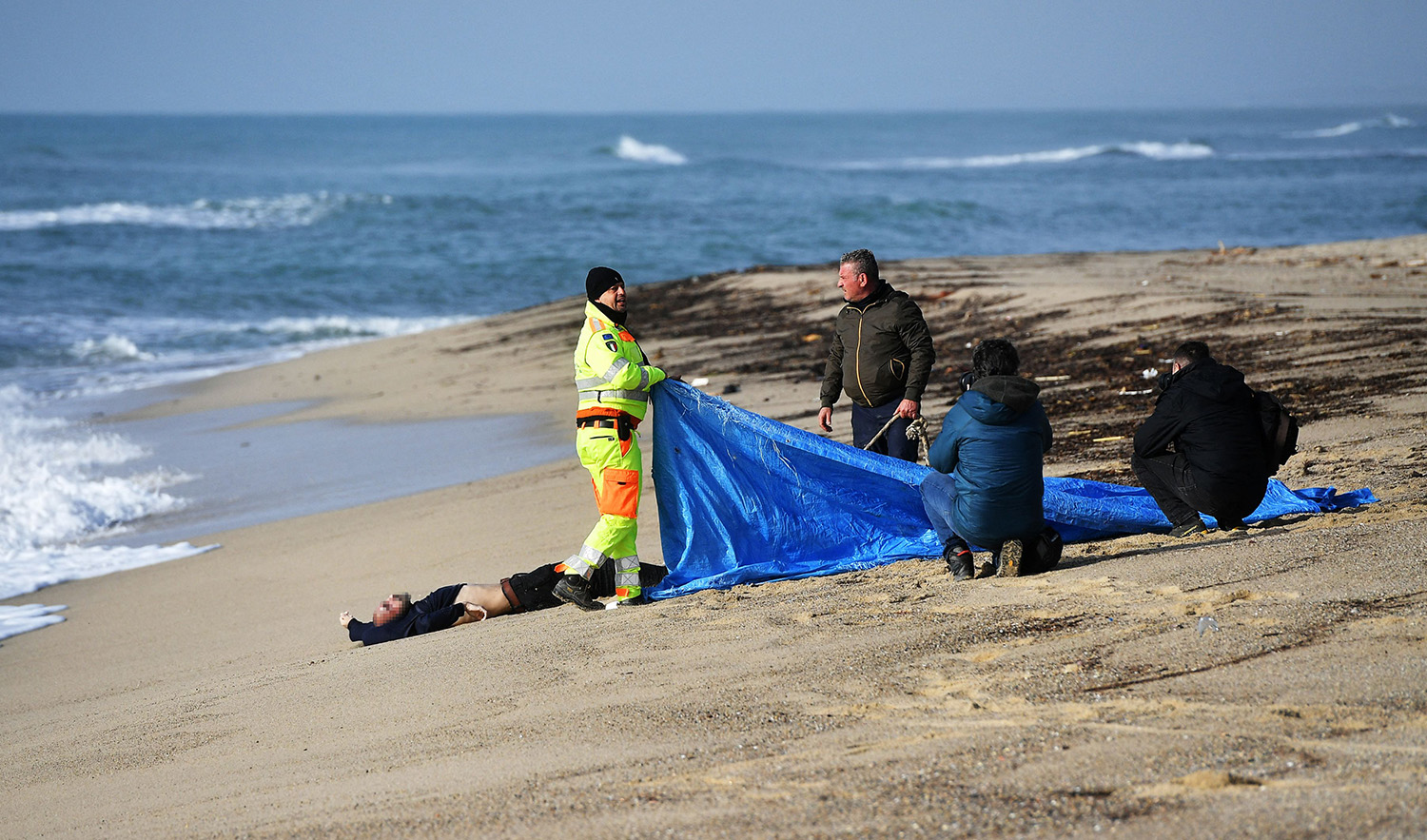 Rescuers cover a body washed up on the beach two days after a boat of migrants sank off Italy's southern Calabria region, in Steccato di Cutro, south of Crotone on February 28, 2023. (AFP)