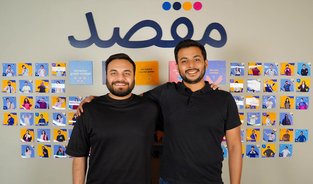 The undated photo shows Taha Ahmed (L) and Rooshan Aziz, co-founders of edtech company 'Maqsad' standing before the logo of their app Maqsad, in Karachi, Pakistan. (Photo courtesy: Maqsad)