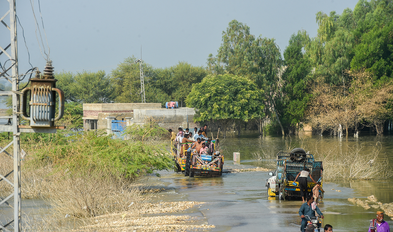 In this picture taken on October 28, 2022, internally displaced people use tractor trolley to wade across a flooded street in Dadu district of Sindh province. (AFP/FILE)