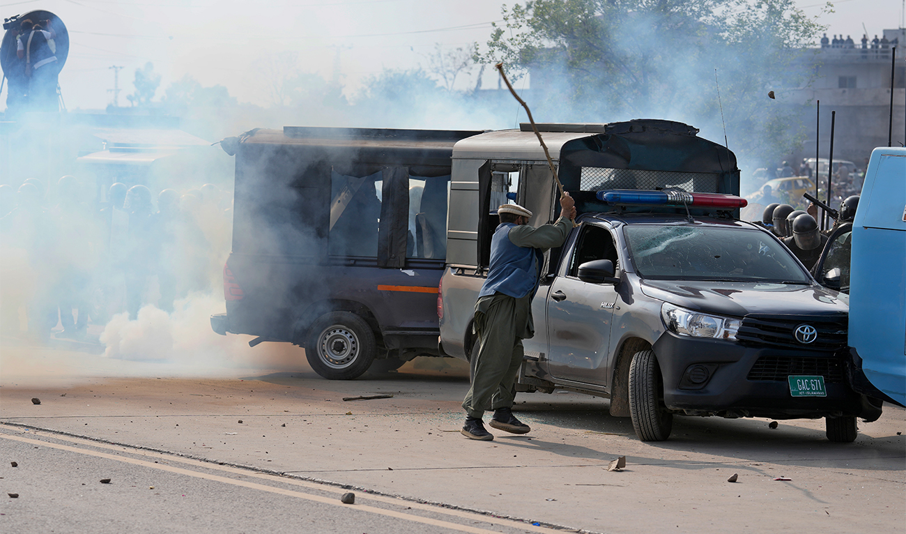 A supporter of former Prime Minister Imran Khan damage a police vehicle as police fire tear gas to disperse them during clashes, in Islamabad, Pakistan, Saturday, March 18, 2023. (AP)