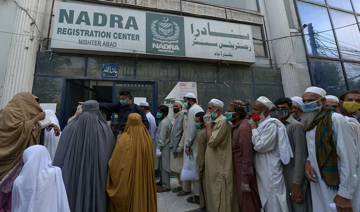 Residents wearing facemasks line up in a queue outside the National Database and Registration Authority (NADRA) office for new registrations and biometric verification under the governmental Ehsaas Emergency Cash Programme for families in need during a government-imposed nationwide lockdown as a preventive measure against the COVID-19 coronavirus, in Peshawar on May 4, 2020. (AFP/FILE)