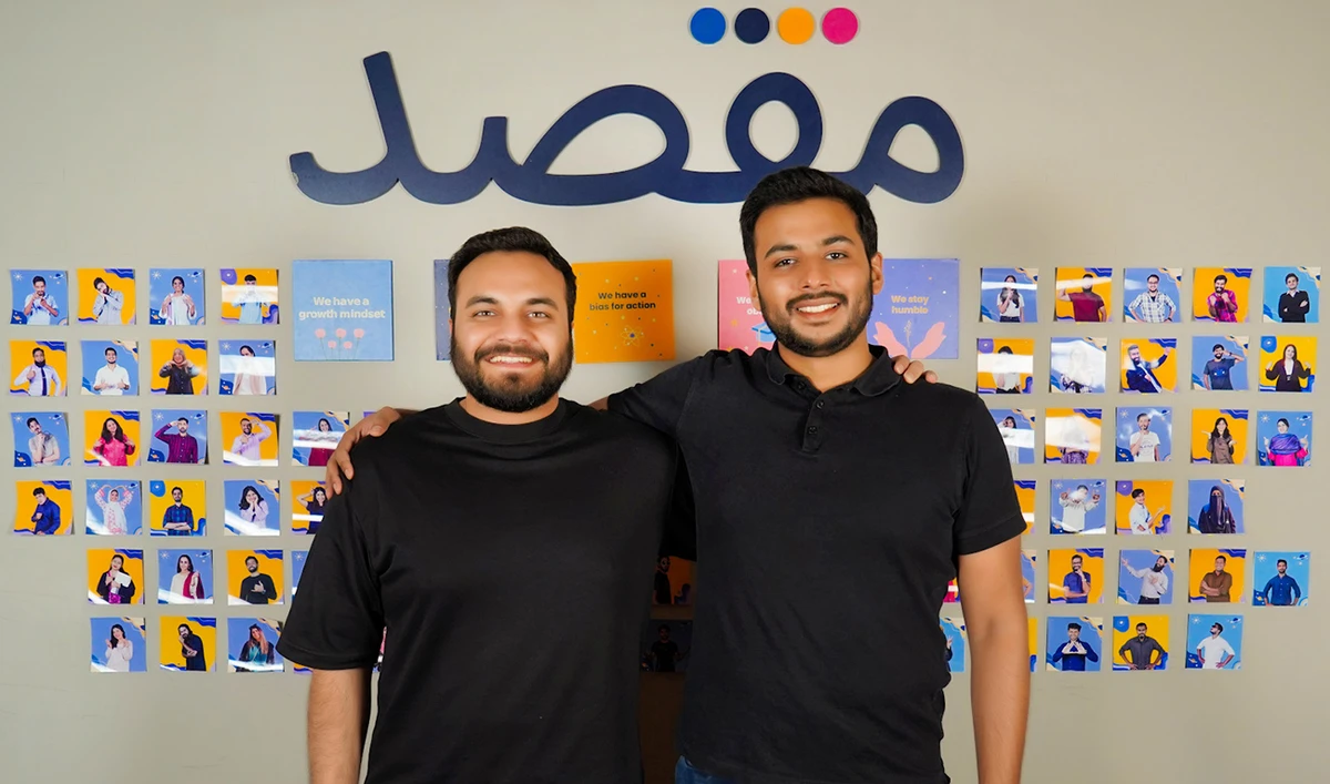 The undated photo shows Taha Ahmed (L) and Rooshan Aziz, co-founders of edtech company 'Maqsad' standing before the logo of their app Maqsad, in Karachi, Pakistan. (Photo courtesy: Maqsad)