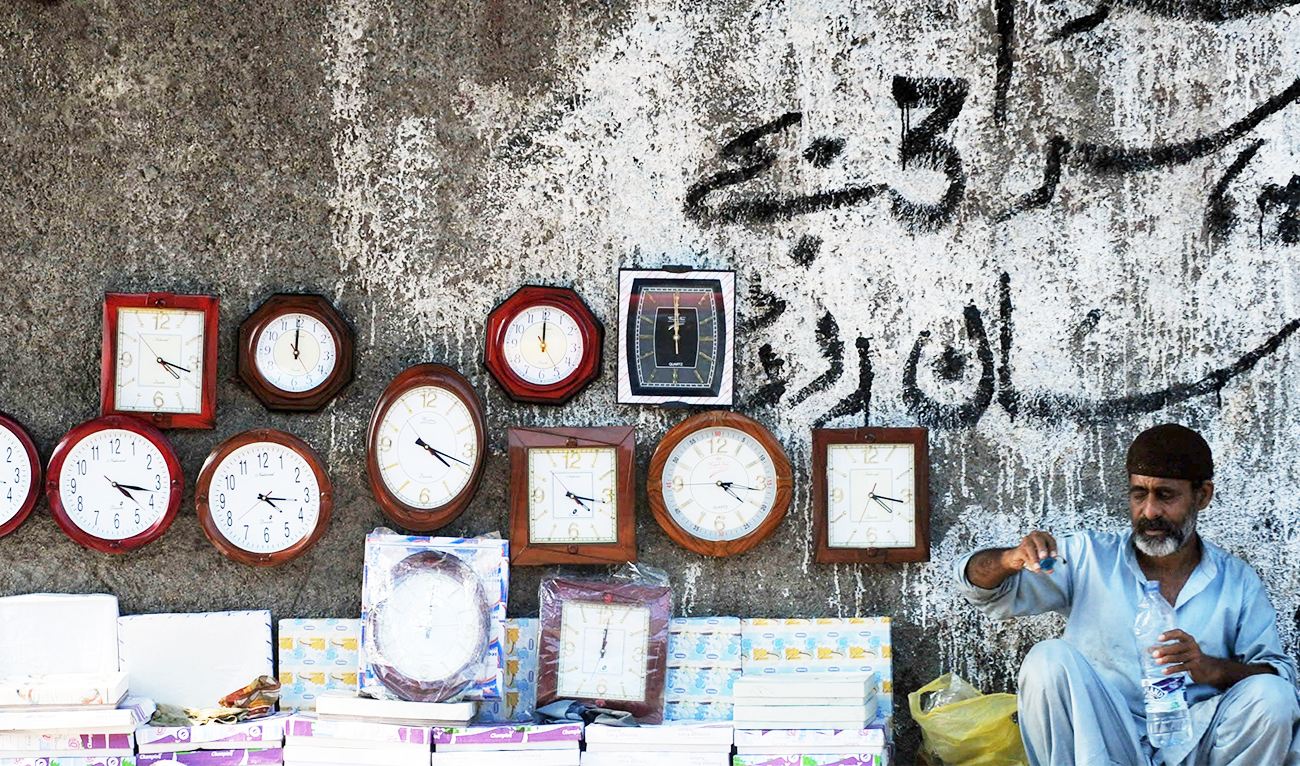 A Pakistani vendor (R) waits for customers as he sells cheap clocks on a footpath in Saddar bazaar, a neighbourhood of Karachi, on March 15, 2010. (AFP /FILE)