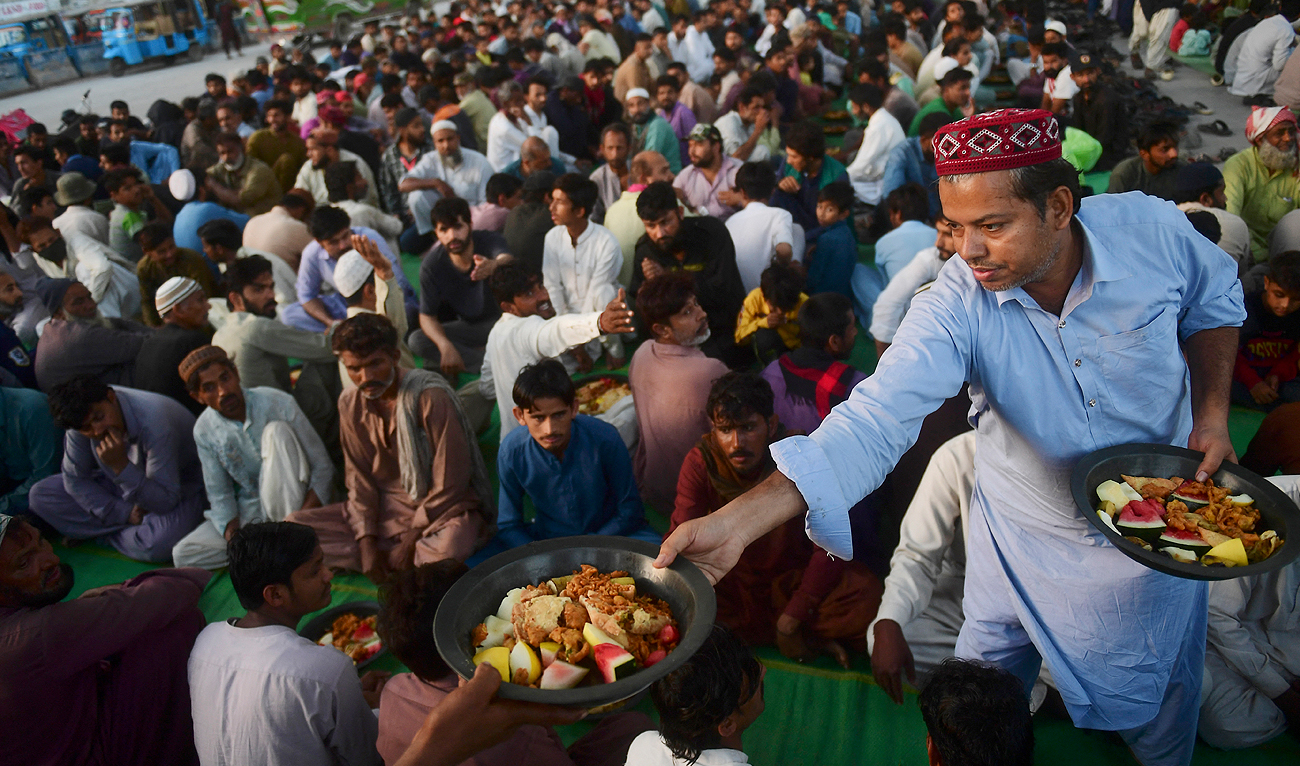 A volunteer gives Iftar food to Muslim devotees as they wait to break their fast along a street on the second day the Holy month of Ramadan in Karachi on March 24, 2023. (Photo courtesy: AFP)