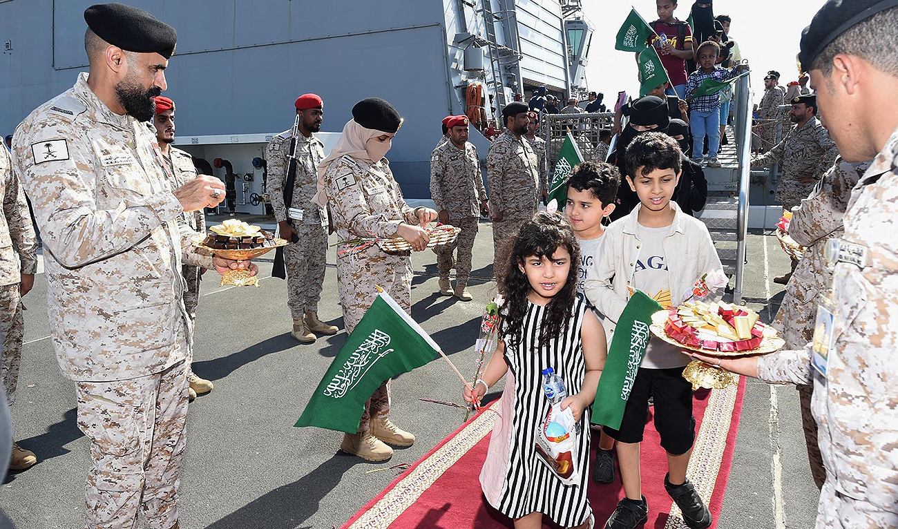 A handout picture provided by the Saudi Press Agency (SPA) on April 22, 2023, shows members of the armed forces passing out chocolates and flowers to Saudi citizens and other nationals upon their arrival in Jeddah, following their rescue from Sudan. (Photo courtesy: SPA)