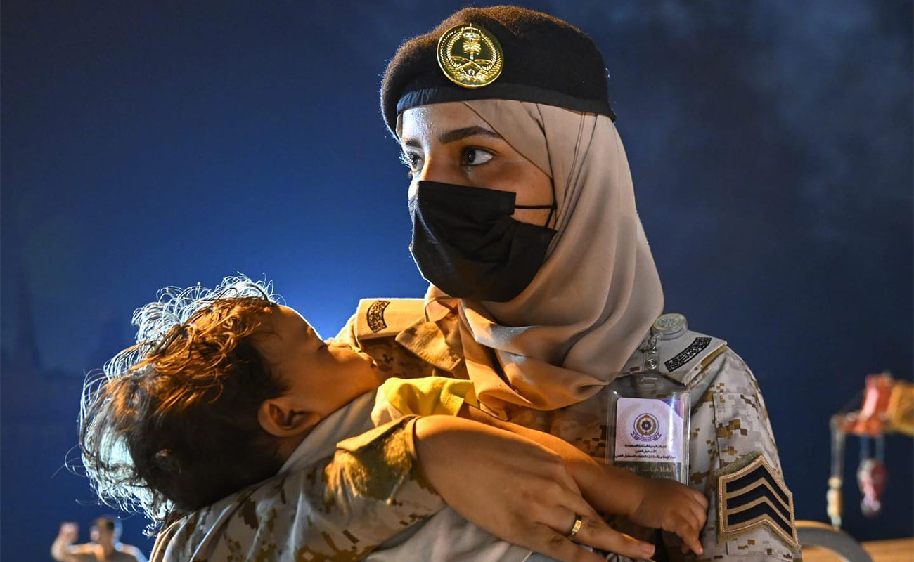 A Saudi Navy sailor carries a child as a Saudi ship transporting evacuees of different nationalities from Sudan arrive at the King Faisal Naval Base in Jeddah on April 24, 2023. (SPA)