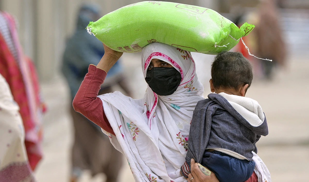 A woman carries her child while she leaves with a free bag of flour from a government distribution point in Islamabad on April 1, 2023. (Photo courtesy: AFP)