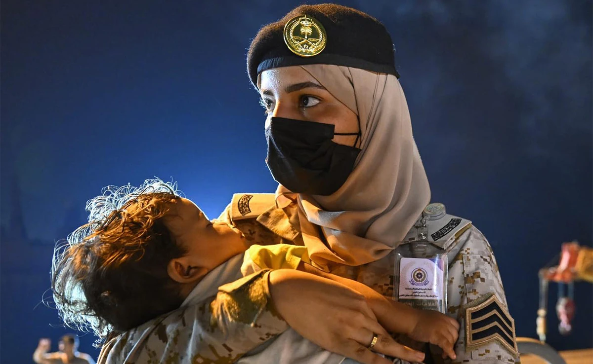 A Saudi Navy sailor carries a child as a Saudi ship transporting evacuees of different nationalities from Sudan arrive at the King Faisal Naval Base in Jeddah on April 24, 2023. (SPA)