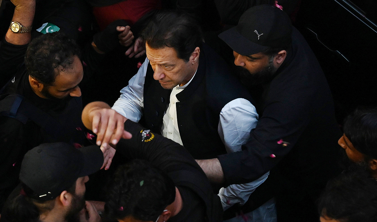 Security personnel escort former Pakistan's Prime Minister Imran Khan as he arrives to appear at the high court in Lahore on March 17, 2023. (AFP/File)