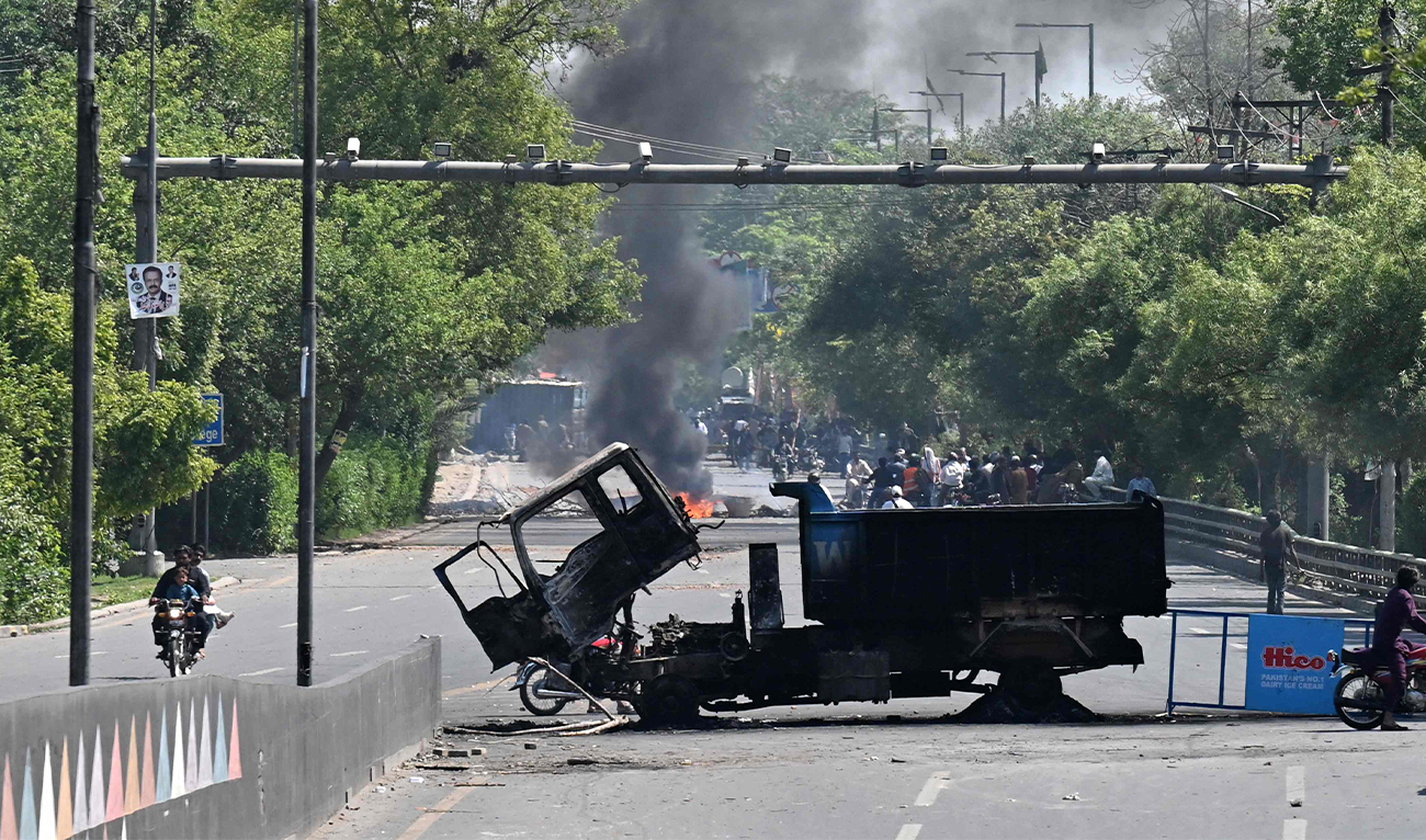Motorists ride past burnt vehicles in front of the Zaman Park, a day after protests by Pakistan Tehreek-e-Insaf (PTI) party activists and supporters of former Pakistan's Prime Minister Imran Khan, in Lahore on May 10, 2023. (AFP)