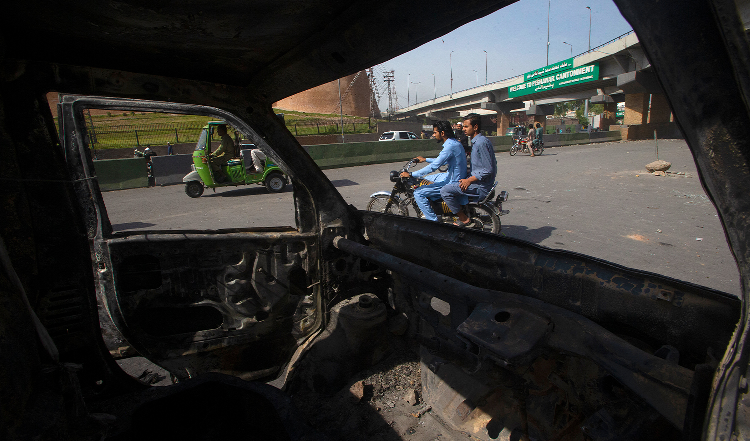 Motorcyclists and rickshaw pullers move past a car burnt in Wednesday's clashes between police and the supporters of Pakistan's former Prime Minister Imran Khan, at a road, in Peshawar, Pakistan, on May 11, 2023. (AP)