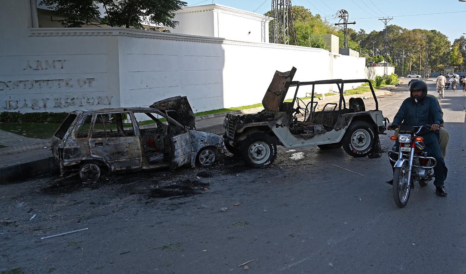 A motorcyclist rides past burnt vehicles in front of the Pakistan Army Institute, a day after protests by Pakistan Tehreek-e-Insaf (PTI) party activists and supporters of former Pakistan's Prime Minister Imran Khan, in Rawalpindi on May 10, 2023. (AFP)