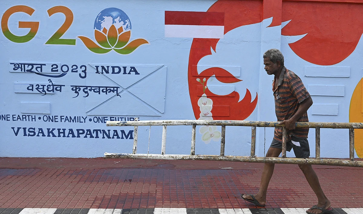 A man walks past a wall mural of the G-20 Summit logo along a street in Visakhapatnam on March 20, 2023. (Photo courtesy: AFP)
