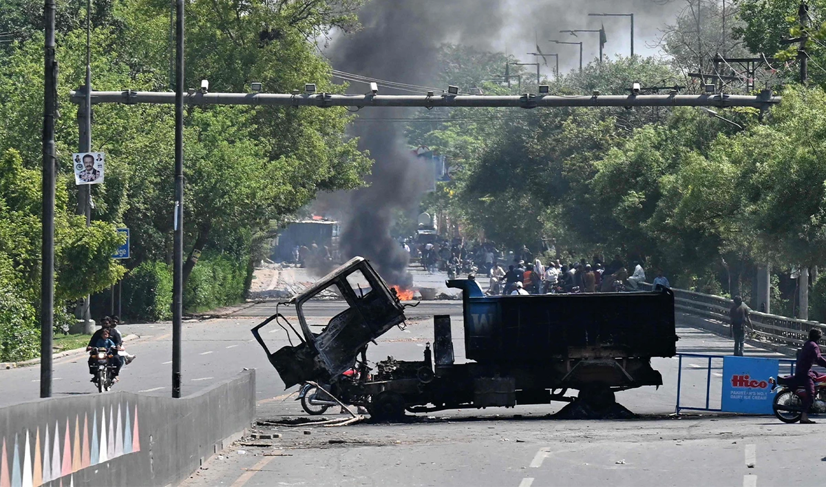Motorists ride past burnt vehicles in front of the Zaman Park, a day after protests by Pakistan Tehreek-e-Insaf (PTI) party activists and supporters of former Pakistan's Prime Minister Imran Khan, in Lahore on May 10, 2023. (AFP)