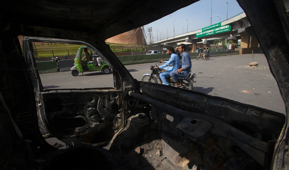 Motorcyclists and rickshaw pullers move past a car burnt in Wednesday's clashes between police and the supporters of Pakistan's former Prime Minister Imran Khan, at a road, in Peshawar, Pakistan, on May 11, 2023. (AP)