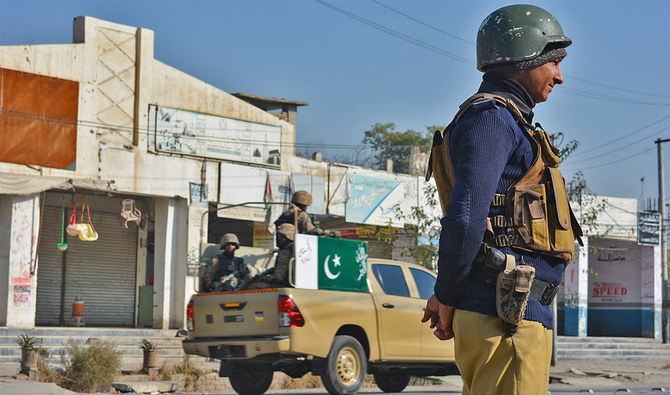 A policeman (R) and army soldiers (L) stand guard along a road in Bannu on December 21, 2022, a day after the seize of a Pakistan police station ended. (AFP/File)