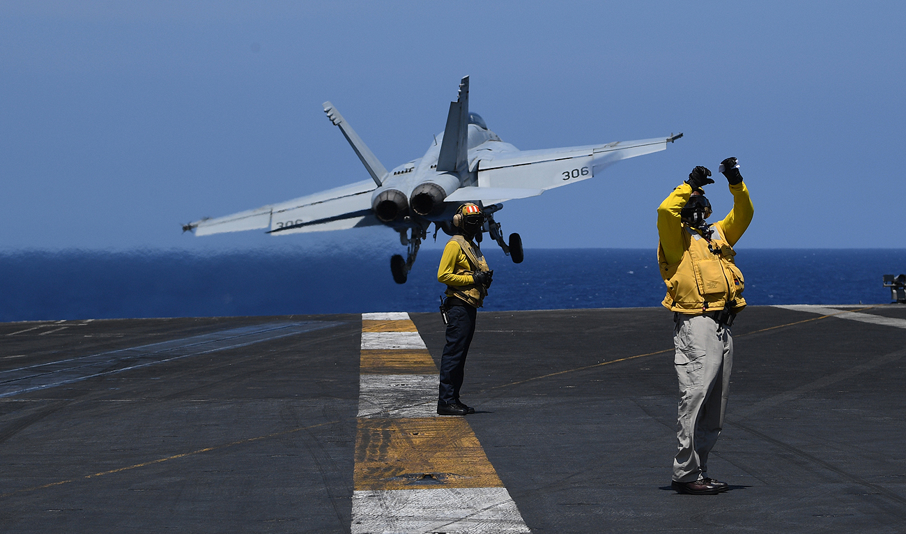 In this photograph, taken on April 10, 2018, US sailors stand on the flight deck while an FA-18 hornet fighter jet takes off, during a routine training aboard US aircraft carrier Theodore Roosevelt in the South China sea. (AFP/File)