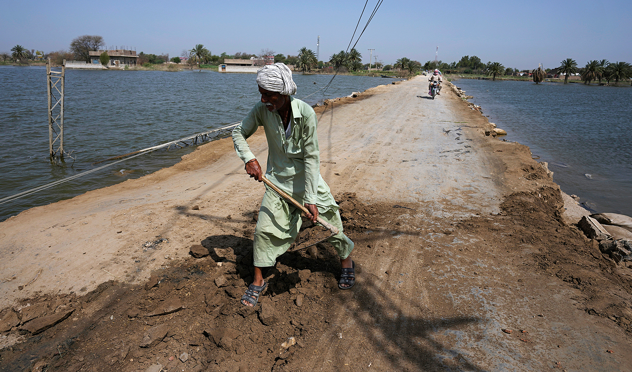 A worker repairs a dusty road surrounded by remaining water of last year's floods, near Therhi town in Khairpur, a district of Pakistan's Sindh province, Saturday, May 20, 2023. (AP)