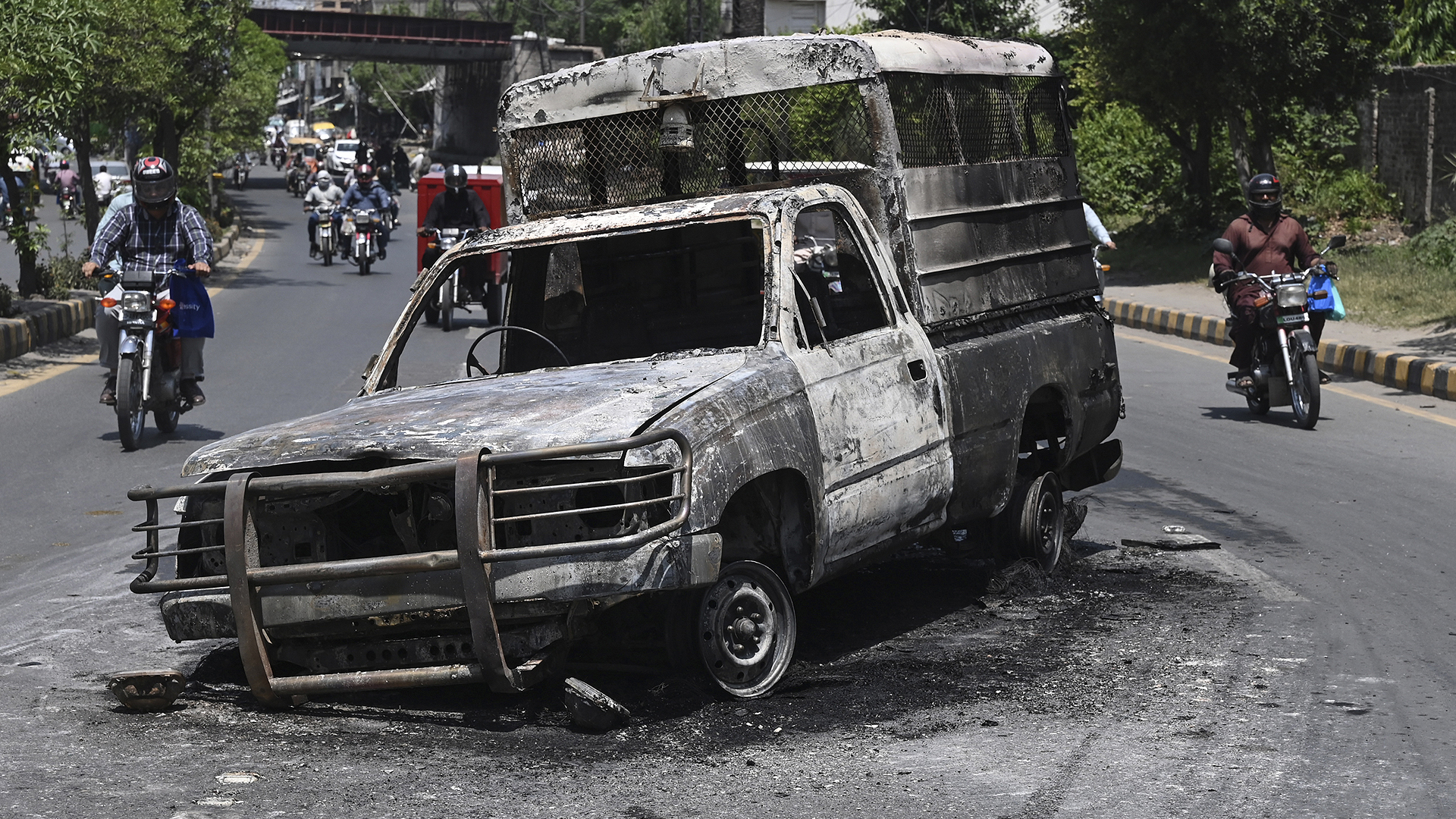 Commuters ride past a burnt vehicle set on fire during a protest by supporters of former Pakistan's Prime Minister Imran Khan over the arrest of their leader, in Lahore on May 11, 2023. (AFP/File)
