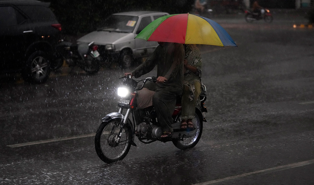 A Pakistani family holds umbrella for their protection as they ride a motorcycle during the rainfall in Lahore, Pakistan, Sunday, June 25, 2023. (AP)