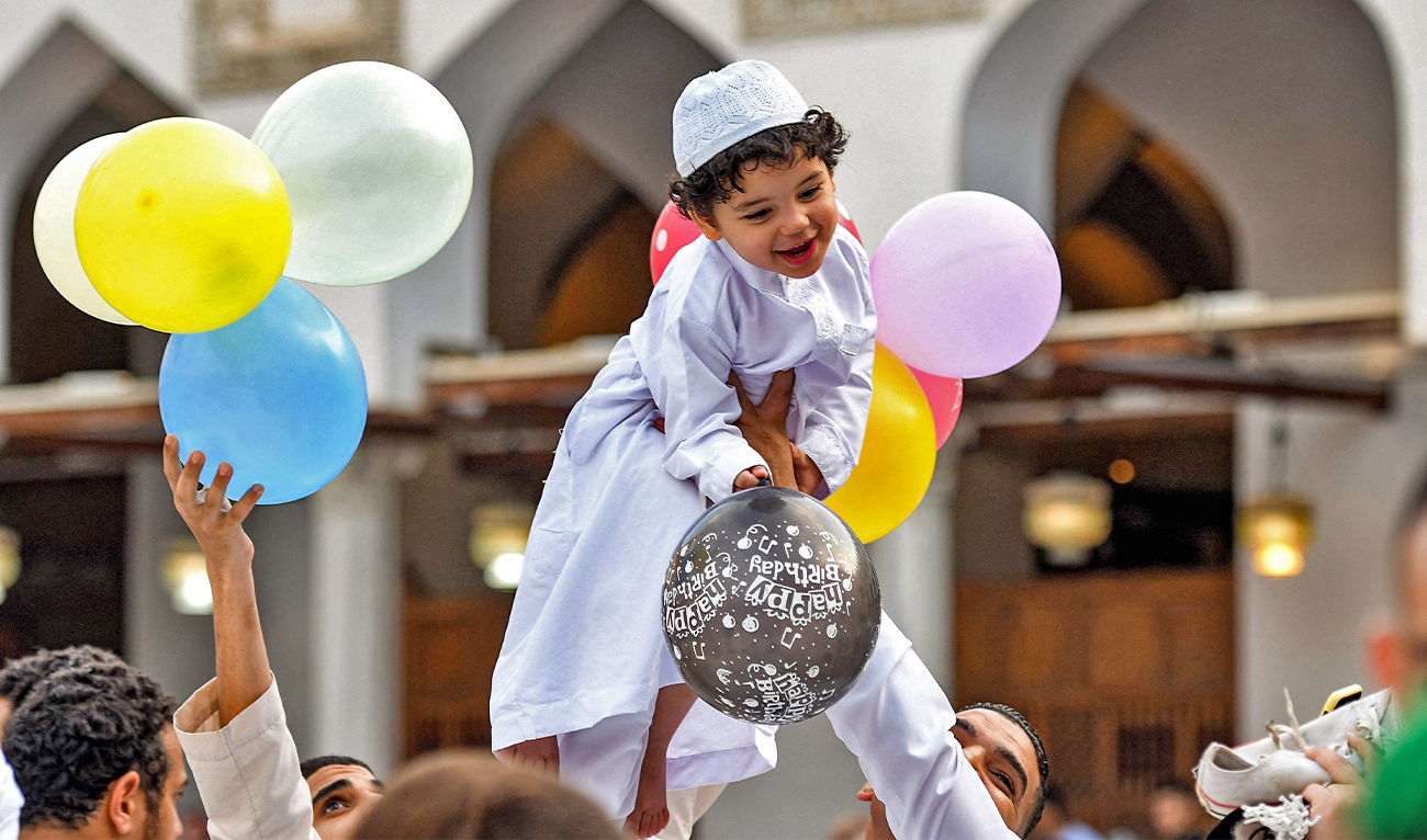 A boy reacts while holding balloons as he is lifted by a man after the morning prayers for Eid al-Adha at the historic Azhar mosque in the centre of Cairo, Egypt, on June 28, 2023. (AFP)