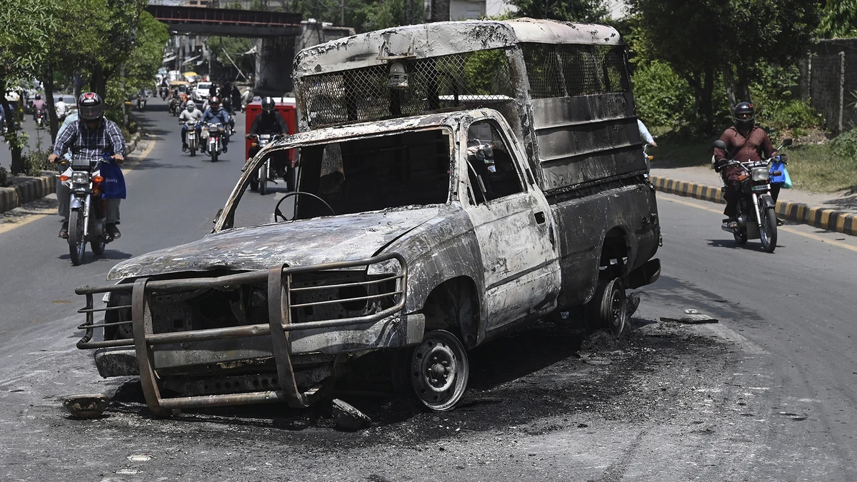 Commuters ride past a burnt vehicle set on fire during a protest by supporters of former Pakistan's Prime Minister Imran Khan over the arrest of their leader, in Lahore on May 11, 2023. (AFP/File)