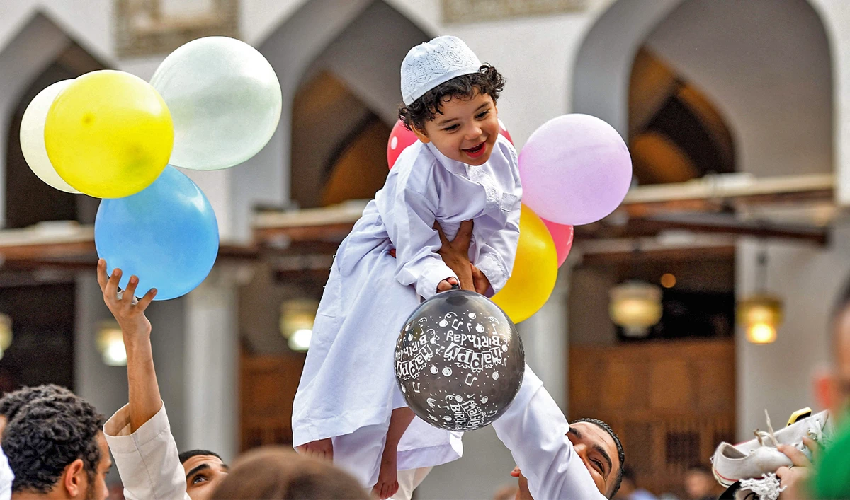 A boy reacts while holding balloons as he is lifted by a man after the morning prayers for Eid al-Adha at the historic Azhar mosque in the centre of Cairo, Egypt, on June 28, 2023. (AFP)