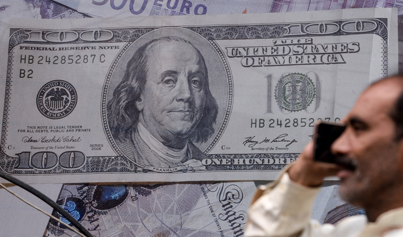 A Pakistani man talks on the phone in front of a poster displaying US dollars at the currency exchange place in Lahore on May 16, 2019. (AFP/File)
