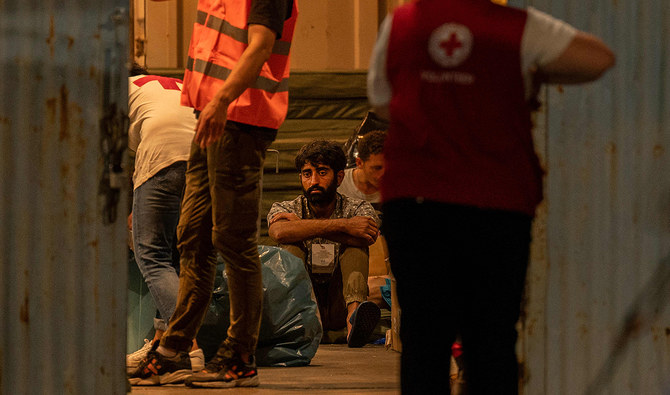 A survivor of a shipwreck sits inside a warehouse next to medical personnel at the port in Kalamata town, on June 14, 2023, after a boat carrying dozens of migrants sank in international waters in the Ionian Sea. (AFP/File)