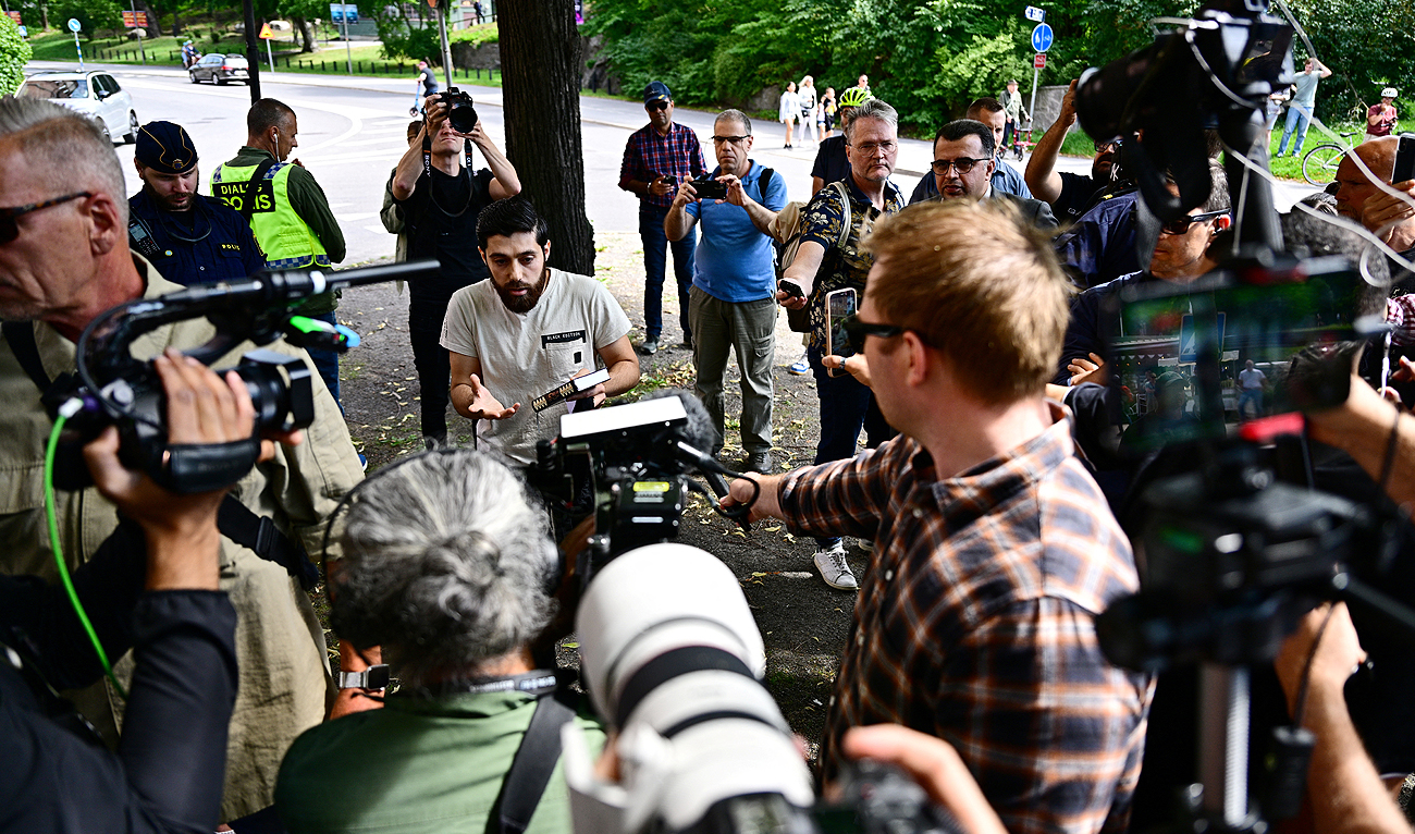 Ahmad A. (C) who has been given permission by the police for a public gathering to burn a Torah and a Bible outside the Israeli embassy in Stockholm, Sweden, is surrounded by journalists on July 15, 2023, after he chose not to burn the books but to hold a manifestation holding a Quran in his hand. (AFP)