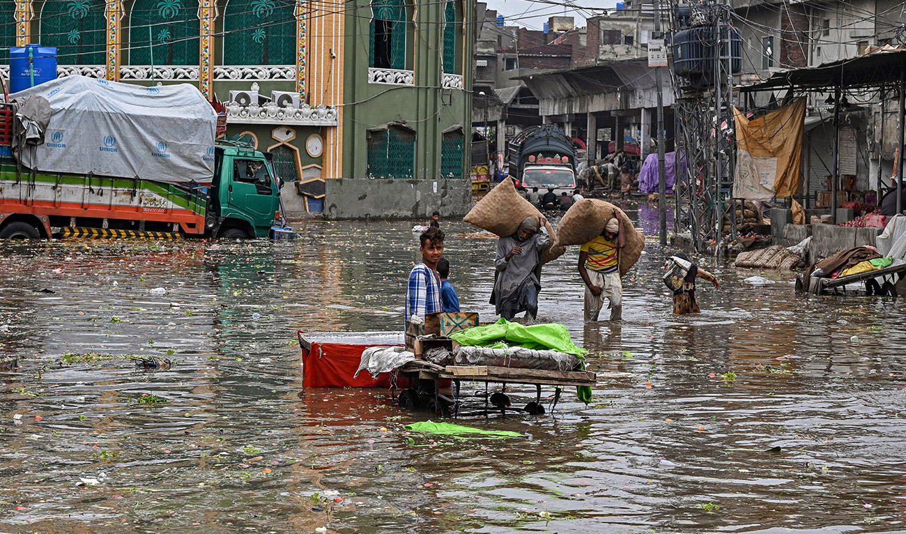 People carry sacks of vegetables as they wade across a flooded market after heavy rainfall in Lahore on June 26, 2023. (AFP/File)