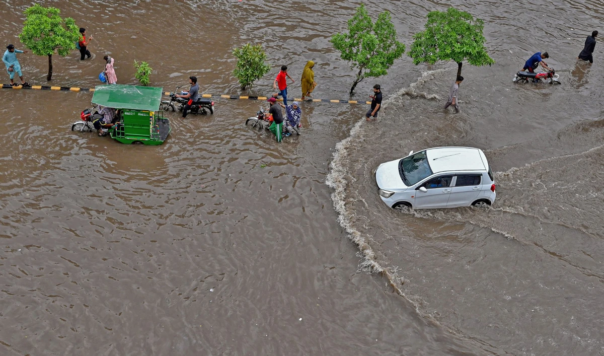 People make their way through a waterlogged road after a heavy rainfall in Lahore on June 26, 2023. (AFP)