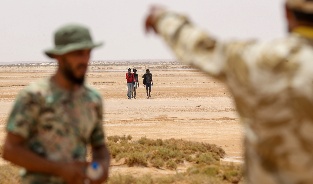 Libyan border guards observe migrants of African origin who reportedly have been abandoned by Tunisian authorities, arriving in an uninhabited area near Al-Assah on the Libya-Tunisia border on July 30, 2023. (AFP/File)