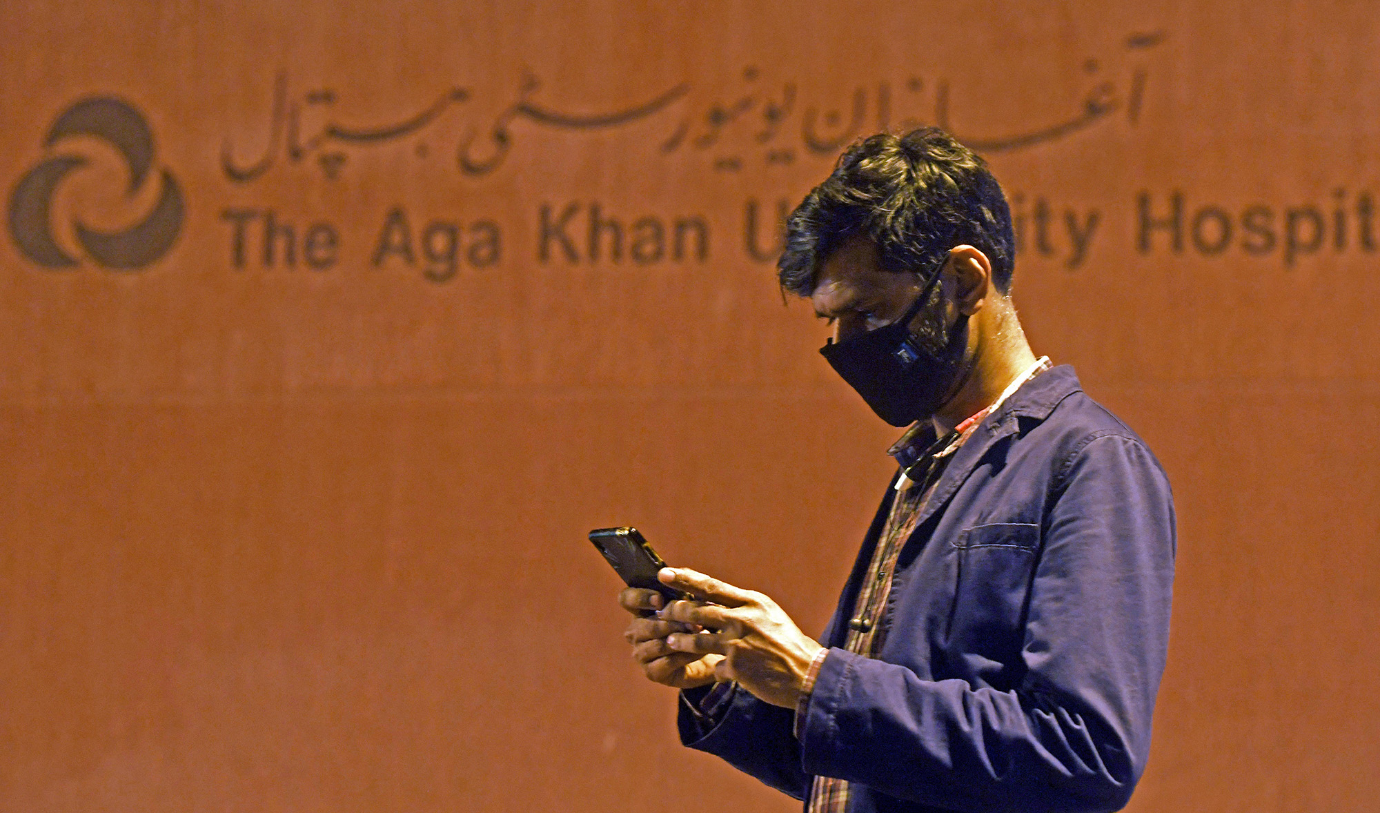 A journalist is seen using his mobile phone outside the Aga Khan University Hospital in Karachi, Pakistan, on February 26, 2020. (AFP/File)