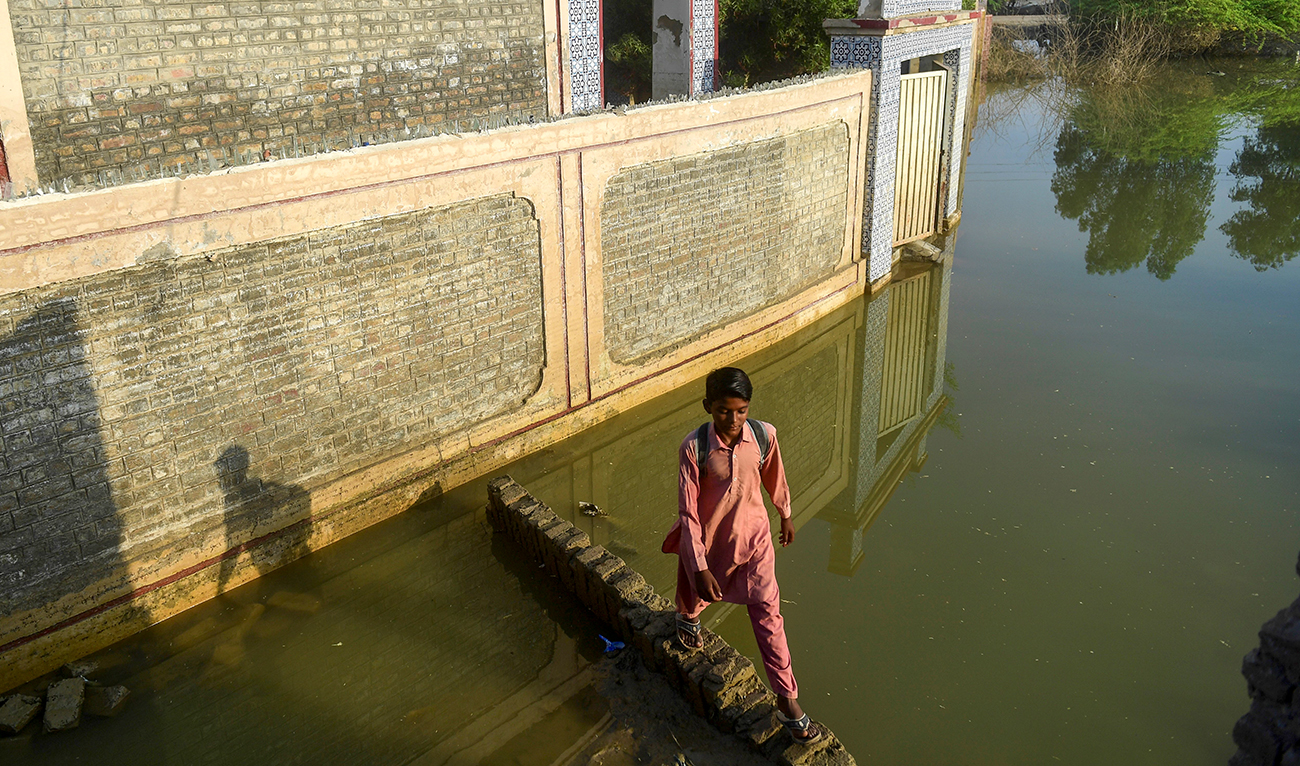 In this picture taken on October 28, 2022, a flood-affected student walks past a deluged government primary school in Chandan Mori, in Dadu district of Sindh province. (AFP/File)