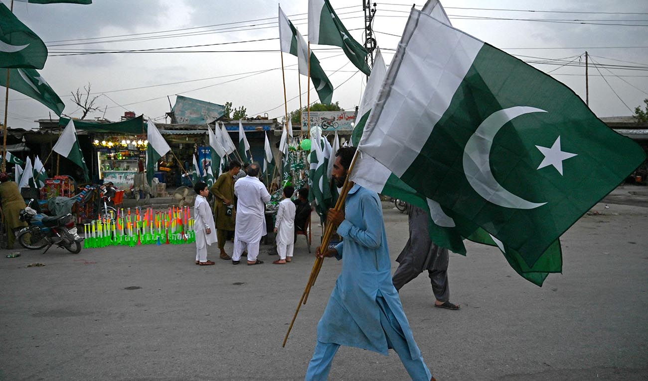 A man carrying Pakistan's national flags, walks through a street on the eve of country's Independence Day celebrations in Peshawar on August 13, 2023. (AFP)