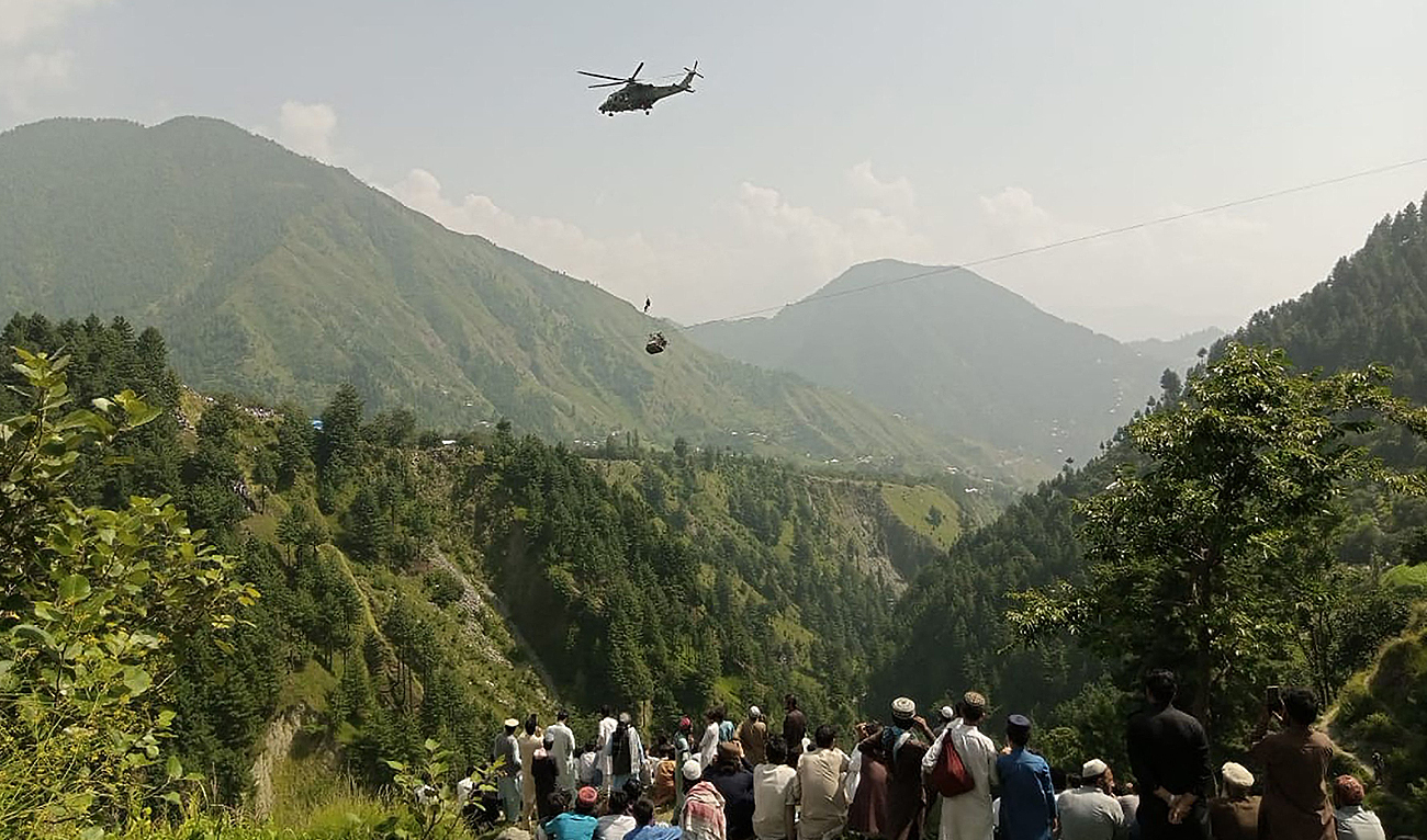 People watch as an army soldier slings down from a helicopter during a rescue mission to recover students stuck in a chairlift in Pashto village of mountainous Khyber Pakhtunkhwa province, on August 22, 2023. (AFP)