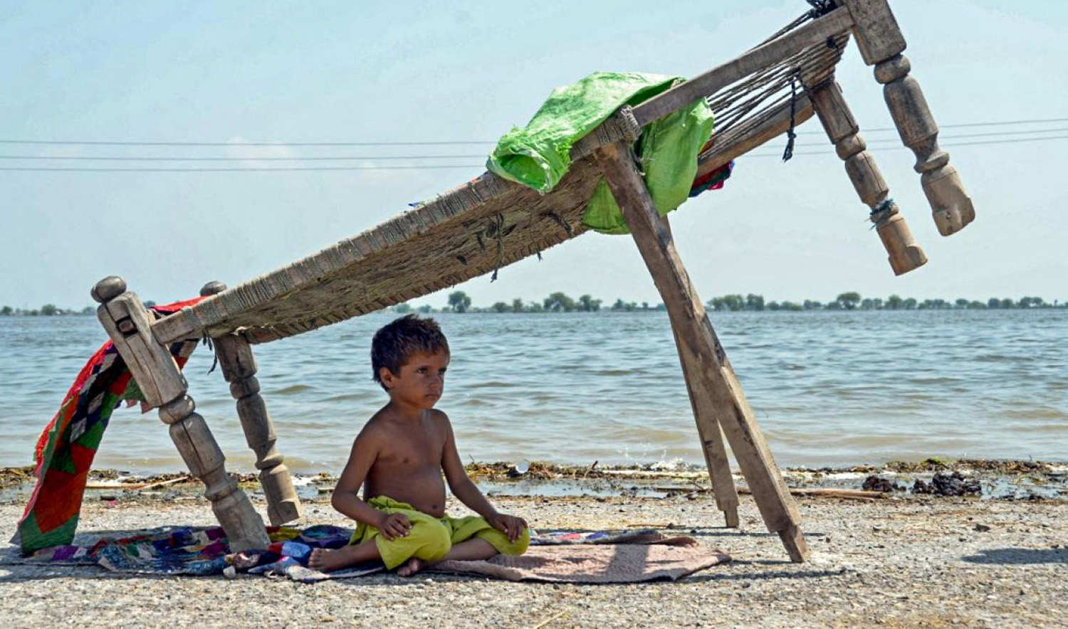 A flood-affected child sits under a charpai near by his family alongside flood waters after heavy monsoon rains in Jaffarabad district of Pakistan's Balochistan province on August 31, 2022. (AFP/File)