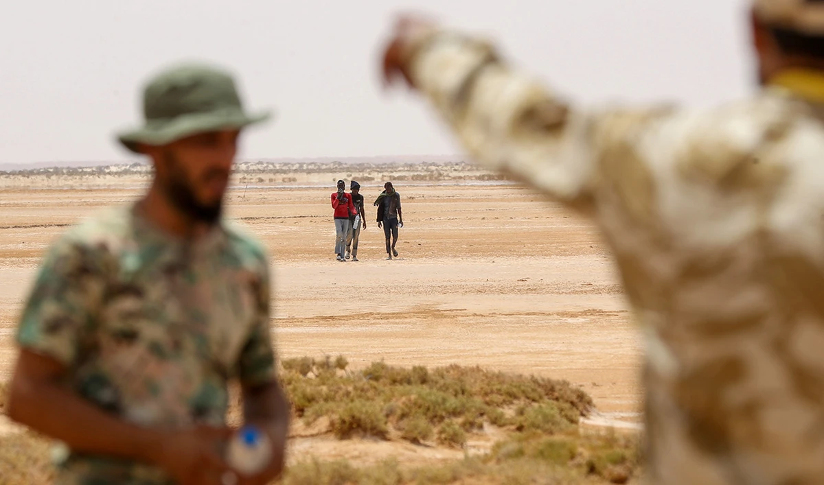 Libyan border guards observe migrants of African origin who reportedly have been abandoned by Tunisian authorities, arriving in an uninhabited area near Al-Assah on the Libya-Tunisia border on July 30, 2023. (AFP/File)